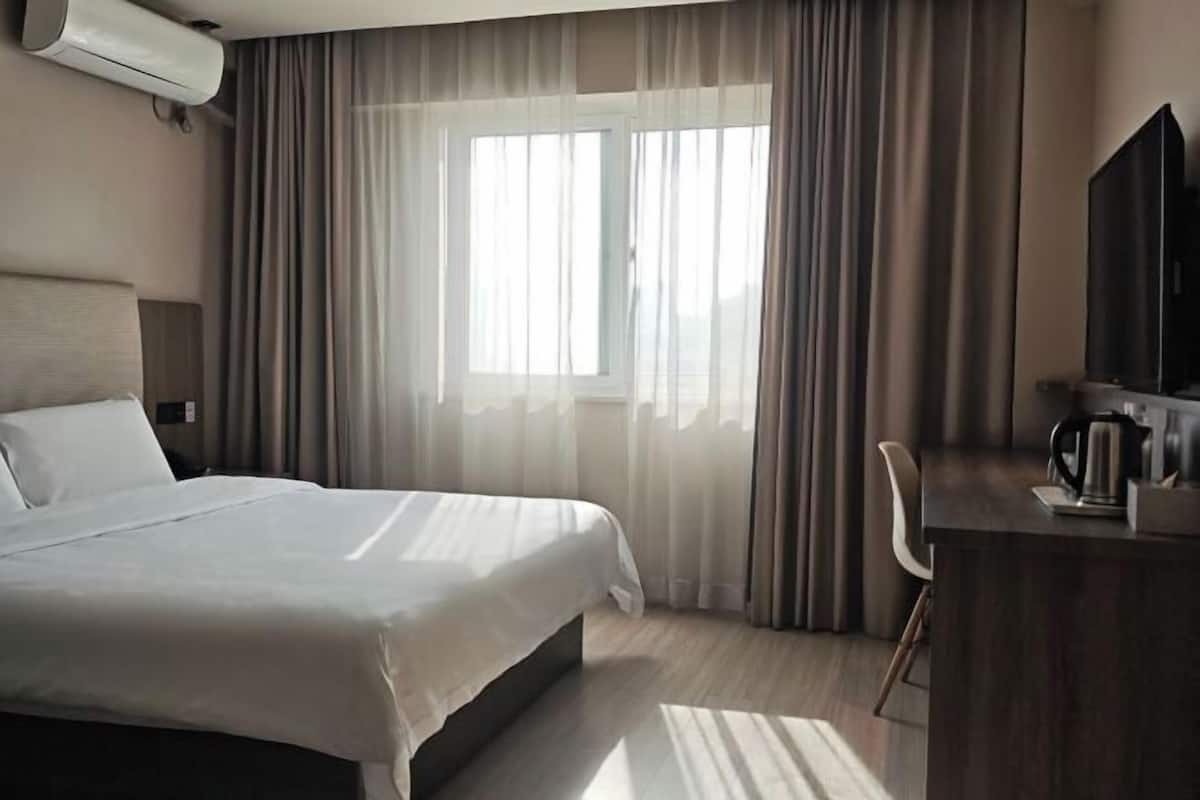 Habitación de hotel con cama, escritorio, silla, televisor y aire acondicionado.