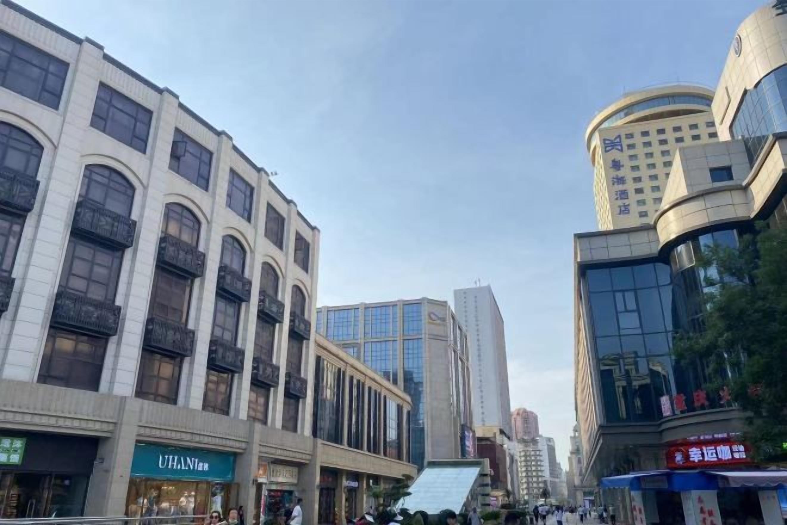 A commercial street with modern buildings, including a UHAAN hotel and a building with a curved facade.