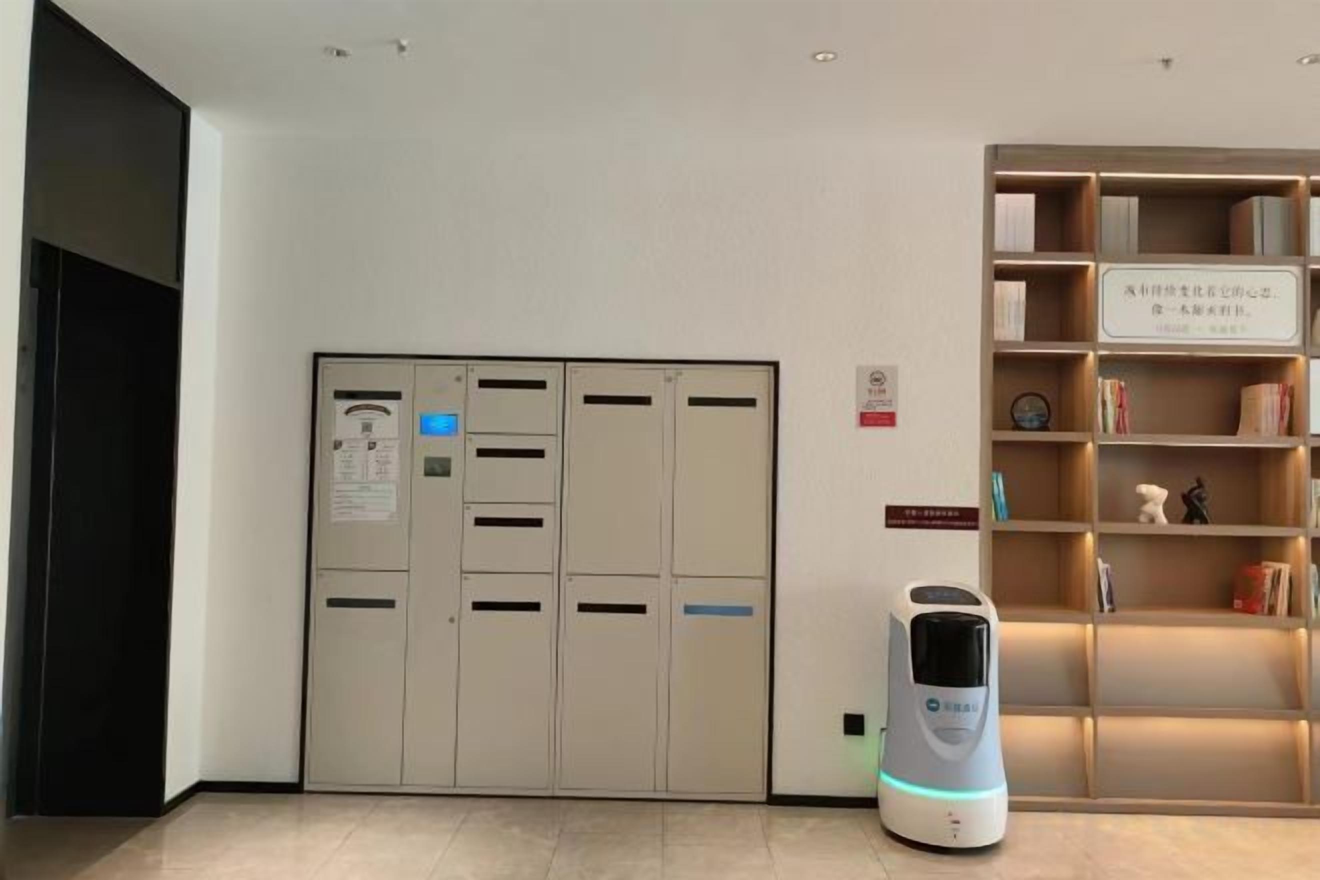 A room with a large, beige, multi-panel door, a white robotic vacuum cleaner, and a wooden bookshelf with various items.