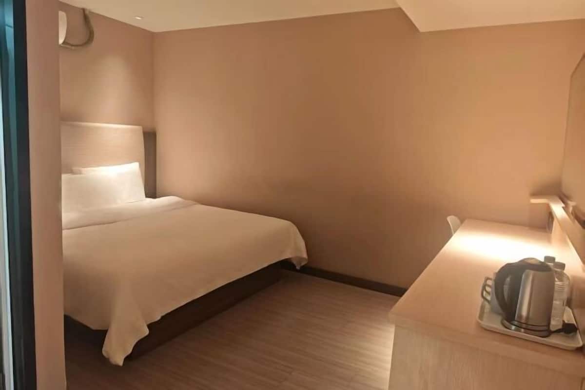 Habitación de hotel con cama, mesita de noche con hervidor y una botella, y una lámpara de pared.