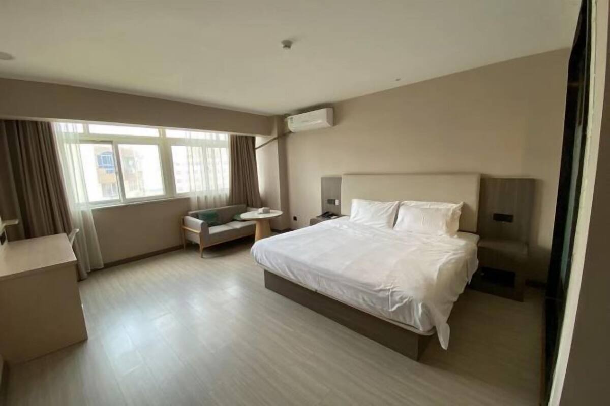 Habitación de hotel con una cama grande, un escritorio, una silla, una mesita y una ventana con cortinas.