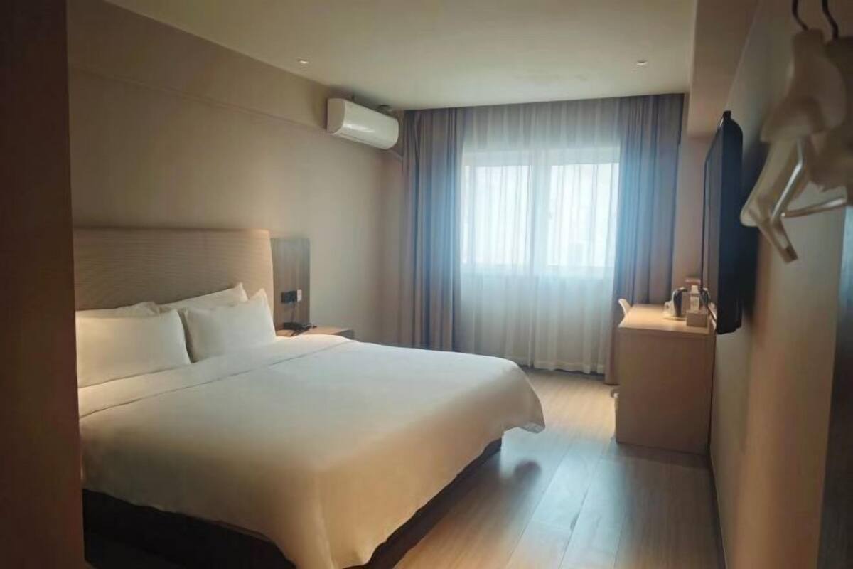 Una habitación de hotel con una cama grande, una mesita de noche, una lámpara y una ventana con cortinas.
