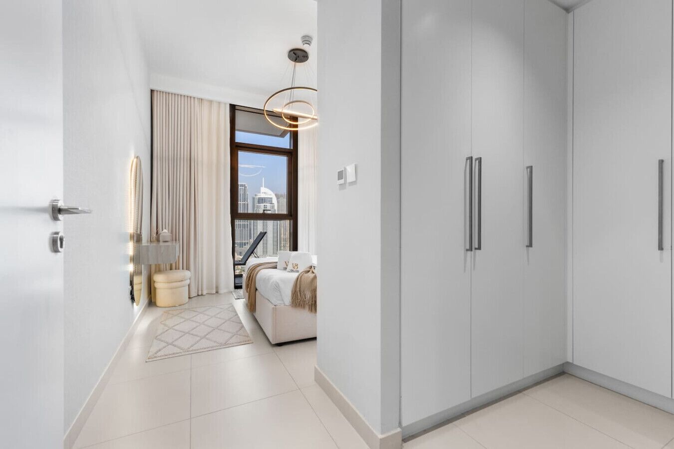 Ett modernt hotellrum med en stor garderob, en säng med utsikt över staden och en minimalistisk inredning.