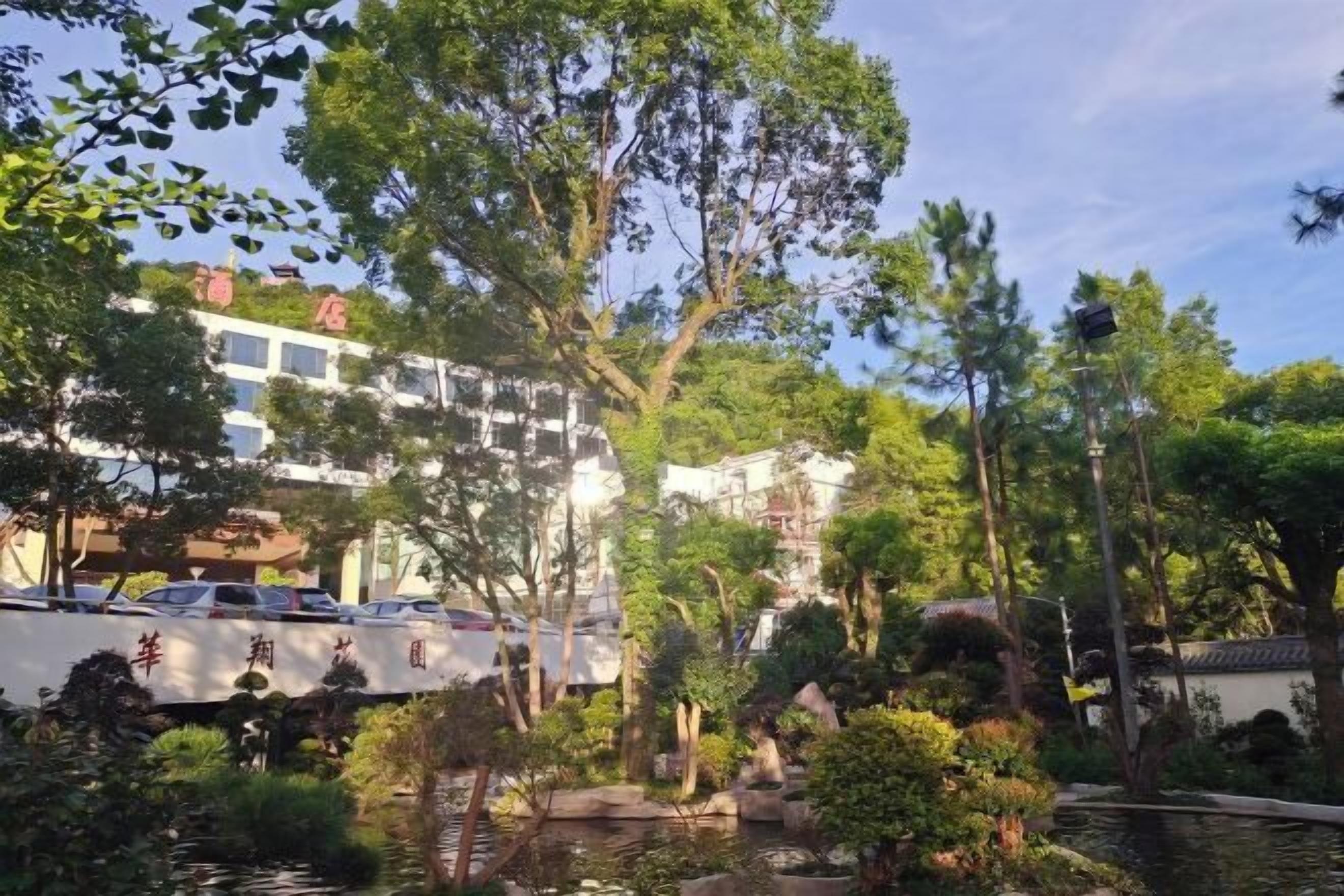 A hotel with a traditional architectural style, surrounded by lush greenery and a small pond.