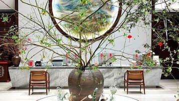 A reception area with a large vase of branches, two wooden chairs, and a circular painting on the wall.