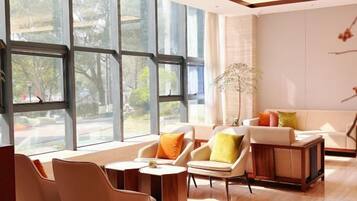 A modern hotel room with large windows, a sofa set, a small table, and a decorative plant.