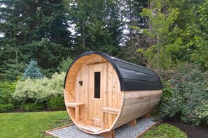 Una sauna de madera con techo curvo, integrada en un jardín con abundante vegetación.