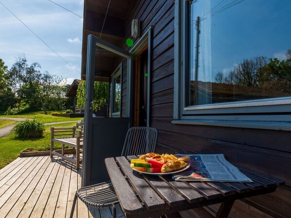 Une terrasse extérieure en bois avec une table, des chaises et une assiette de nourriture.