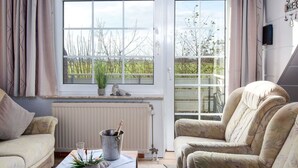 Uma sala de estar acolhedora com sofá, poltrona e uma mesa com champanhe, copos e uma planta.