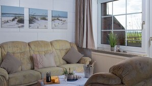 Uma sala de estar aconchegante com um conjunto de sofás, uma mesa de centro com uma garrafa e copos, e uma janela com vista para o exterior.