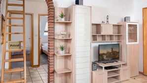 Uma sala de estar com televisão, prateleiras de madeira, uma escada e uma placa com a inscrição 'Privat'.