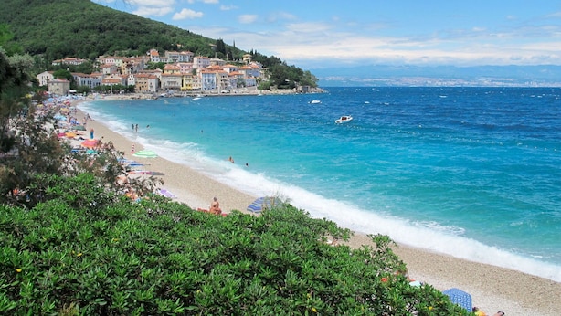 Un pueblo costero con playa, aguas azules cristalinas y edificios a lo largo de la orilla.
