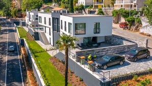 A modern two-story building with a flat roof, a covered patio, and a parking area with cars.