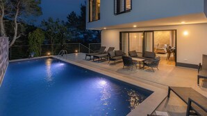 A modern two-story house with a swimming pool, outdoor seating, and a dining area.