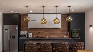 A modern kitchen with a central island, bar stools, a dining table, and built-in appliances.