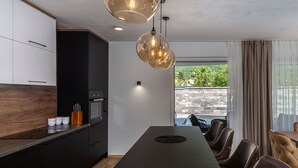 A modern kitchen with dark cabinets, a wooden countertop, and a dining area with leather chairs and a long table.