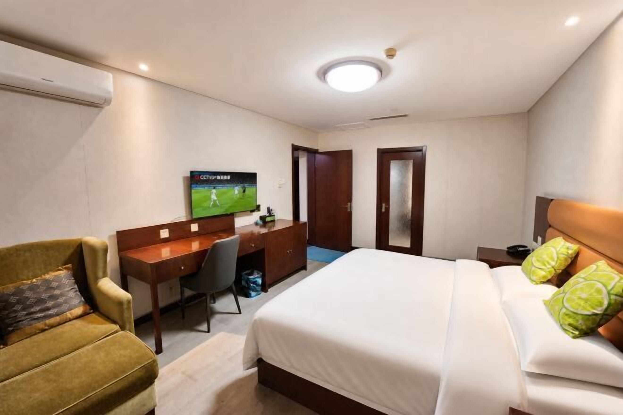 A hotel room with a bed, a desk, a chair, a television, and a door.