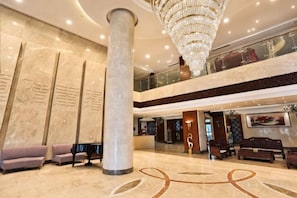 Un hall d’entrée orné de colonnes en marbre, doté d’un lustre, de coins salon et d’un comptoir d’accueil.
