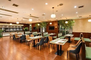 A restaurant with wooden flooring, multiple dining tables and chairs, pendant lighting, and a kitchen area in the background.