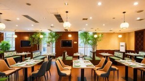 Un restaurant doté de nombreuses tables et de banquettes, d’un éclairage au plafond et de plantes en pot.