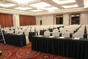 A conference room with rows of tables, white chairs, and a red carpet.