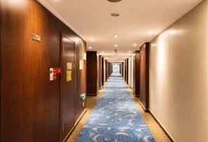 A hotel hallway with wooden doors, a blue patterned carpet, and a long corridor.
