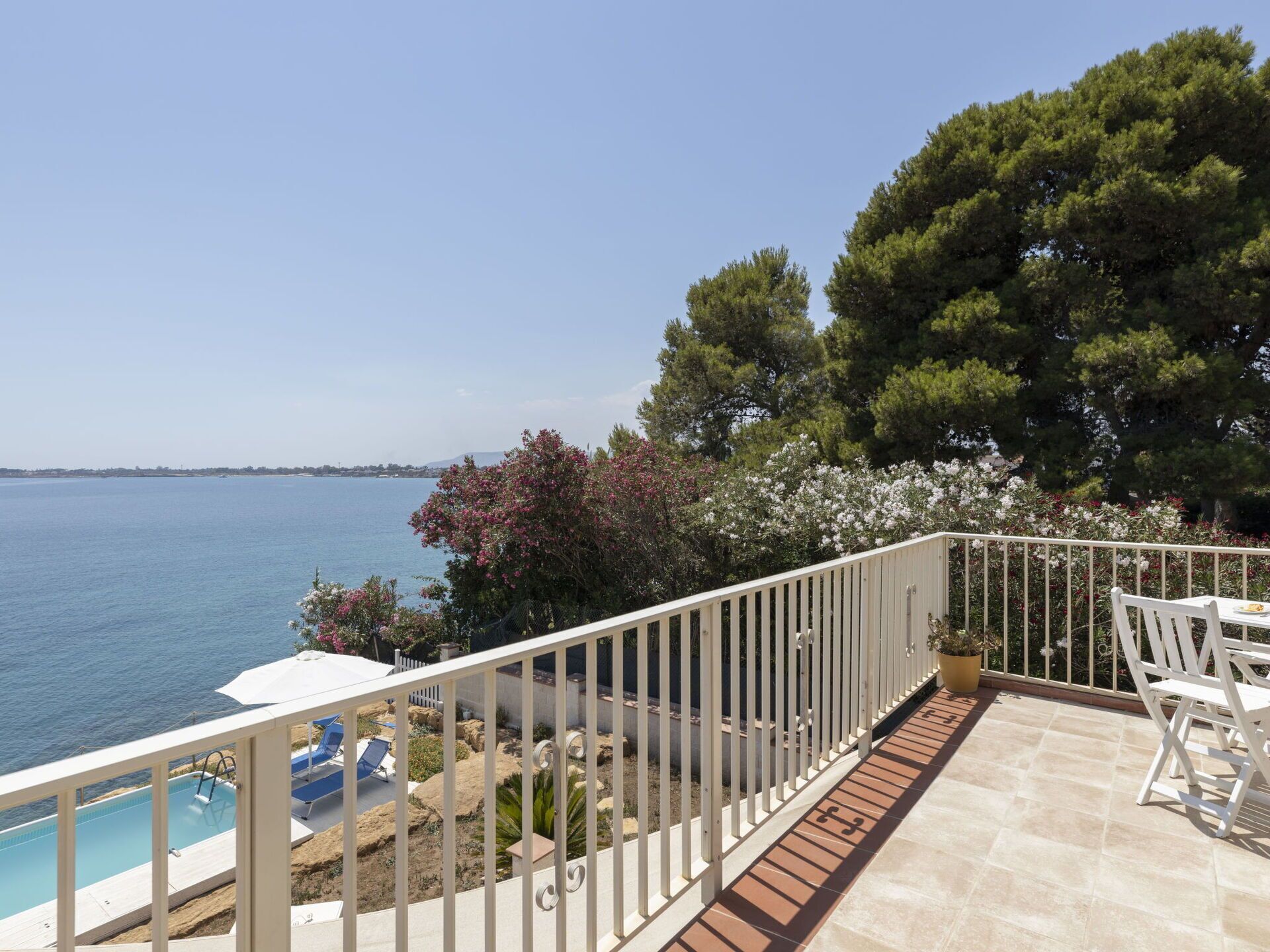 Un balcón con piscina, mobiliario exterior y vista al mar.