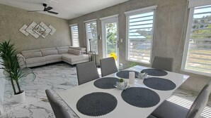 Un espace repas moderne avec une table blanche, des chaises grises et un ventilateur de plafond.