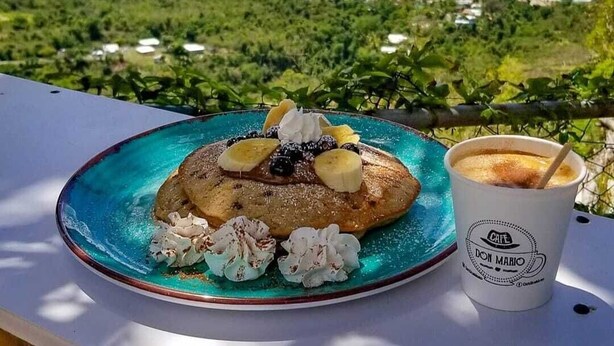 Une table avec une assiette de nourriture et une boisson, donnant sur un paysage côtier.