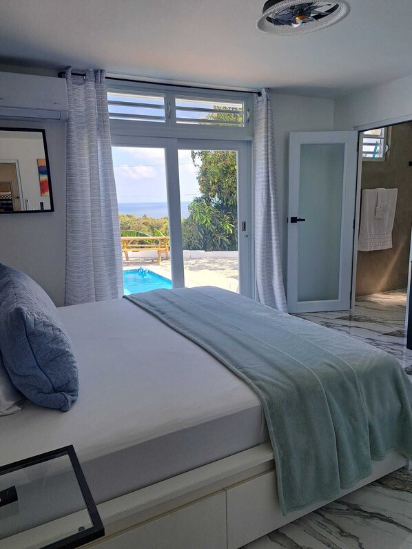 A bedroom with a large bed, a view of a swimming pool, and a door leading to a balcony.