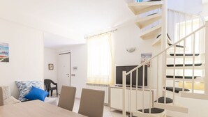 A modern living room with a dining table, chairs, a sofa, a TV, and a spiral staircase. - Stunning private villa for 5 guests with WIFI, A/C, TV, patio and pets allowed (Castiglione Della Pescaia)