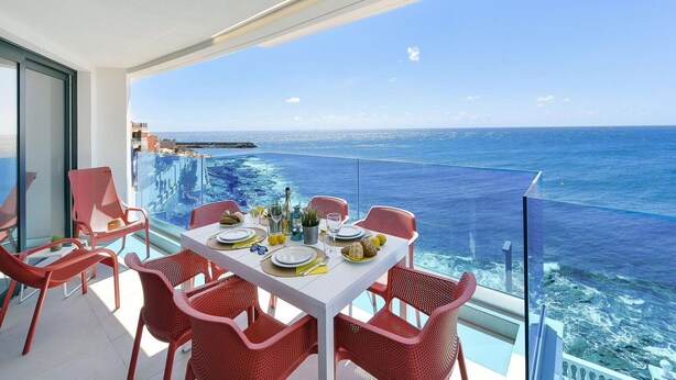 A balcony with a table set for dining, overlooking a clear blue sea and a distant shoreline. - Cosy apartment for 6 people with WIFI, A/C, TV and patio (Telde)
