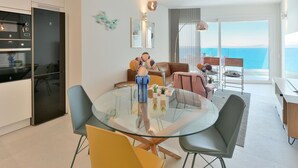 A modern living room with a glass dining table, comfortable seating, a kitchen area with appliances, and a balcony with a view of the sea. - Cosy apartment for 6 people with WIFI, A/C, TV and patio (Telde)