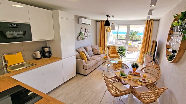 Una cocina compacta con electrodomésticos modernos, una zona de comedor con sillas de mimbre y un sofá.