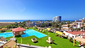 Un resort con varias piscinas, vista a la playa y un paisaje urbano al fondo.