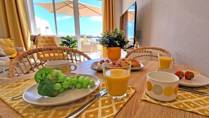 Una mesa de desayuno con platos de uvas, jugo de naranja y fresas, un vaso de jugo de naranja y una taza.