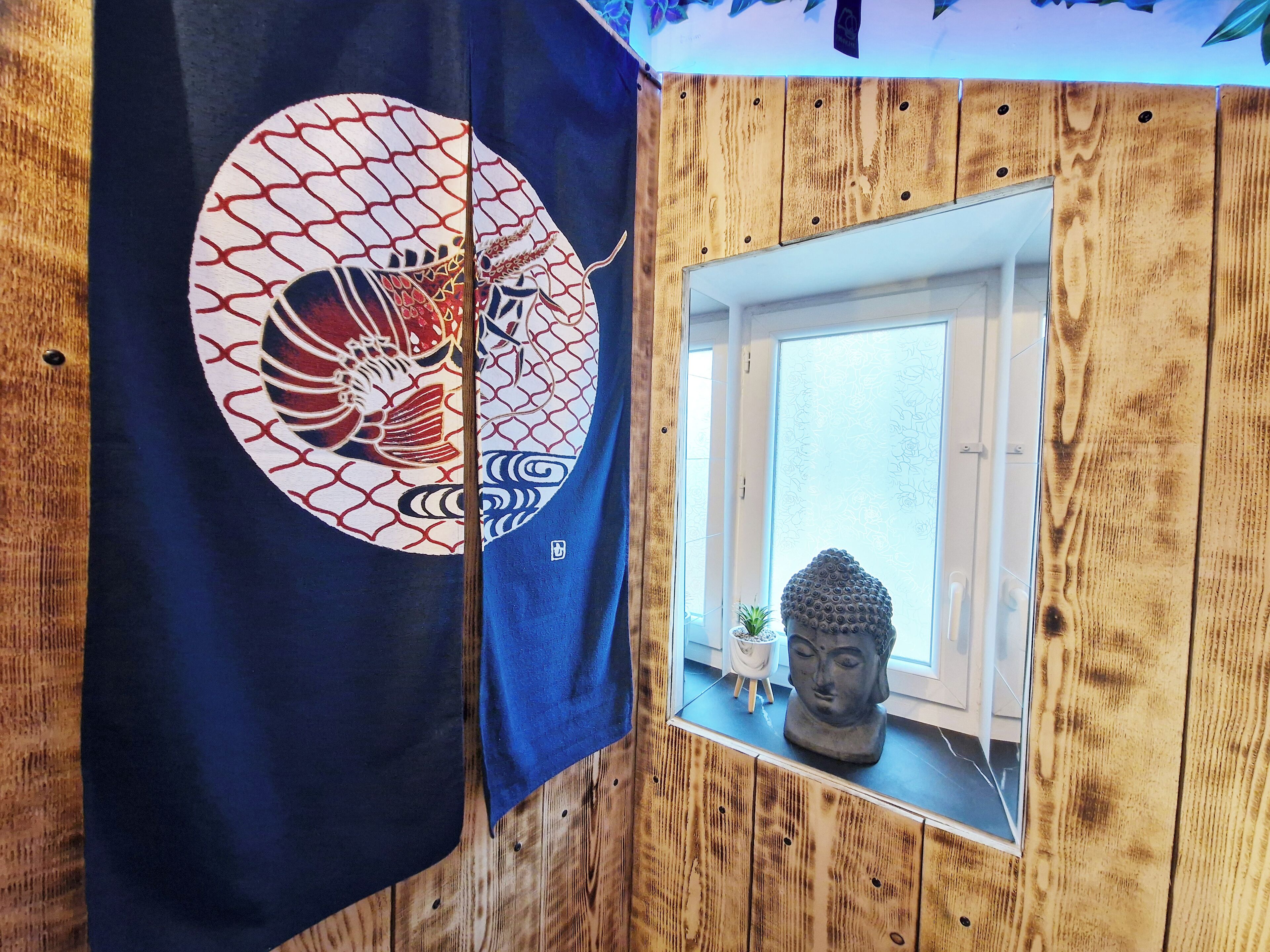 Ett rum med en väggpanel av trä, ett fönster med en Buddha-staty och en vävbonad i japansk stil.