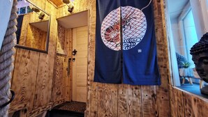 Een houten interieur met een ingang van tatami-matten, een hangend Japans kunstwerk en een Boeddhabeeld.