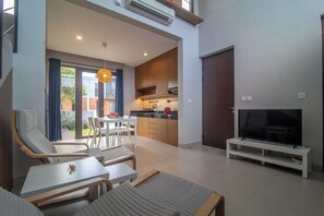 A modern living room with a TV, seating area, and a kitchen in the background. - Grace Villa (Tabanan)