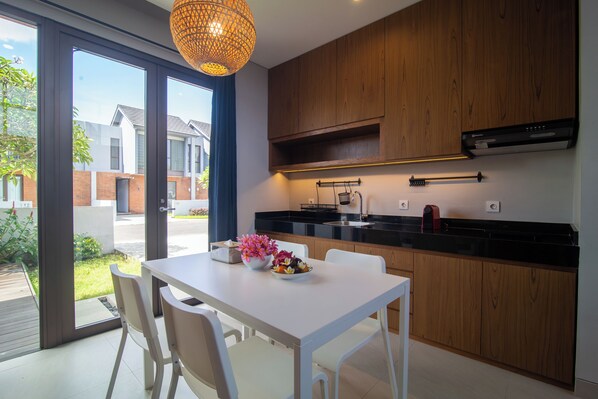 A modern kitchen with wooden cabinets, a white countertop, and a dining area with a white table and chairs. - Grace Villa (Tabanan)