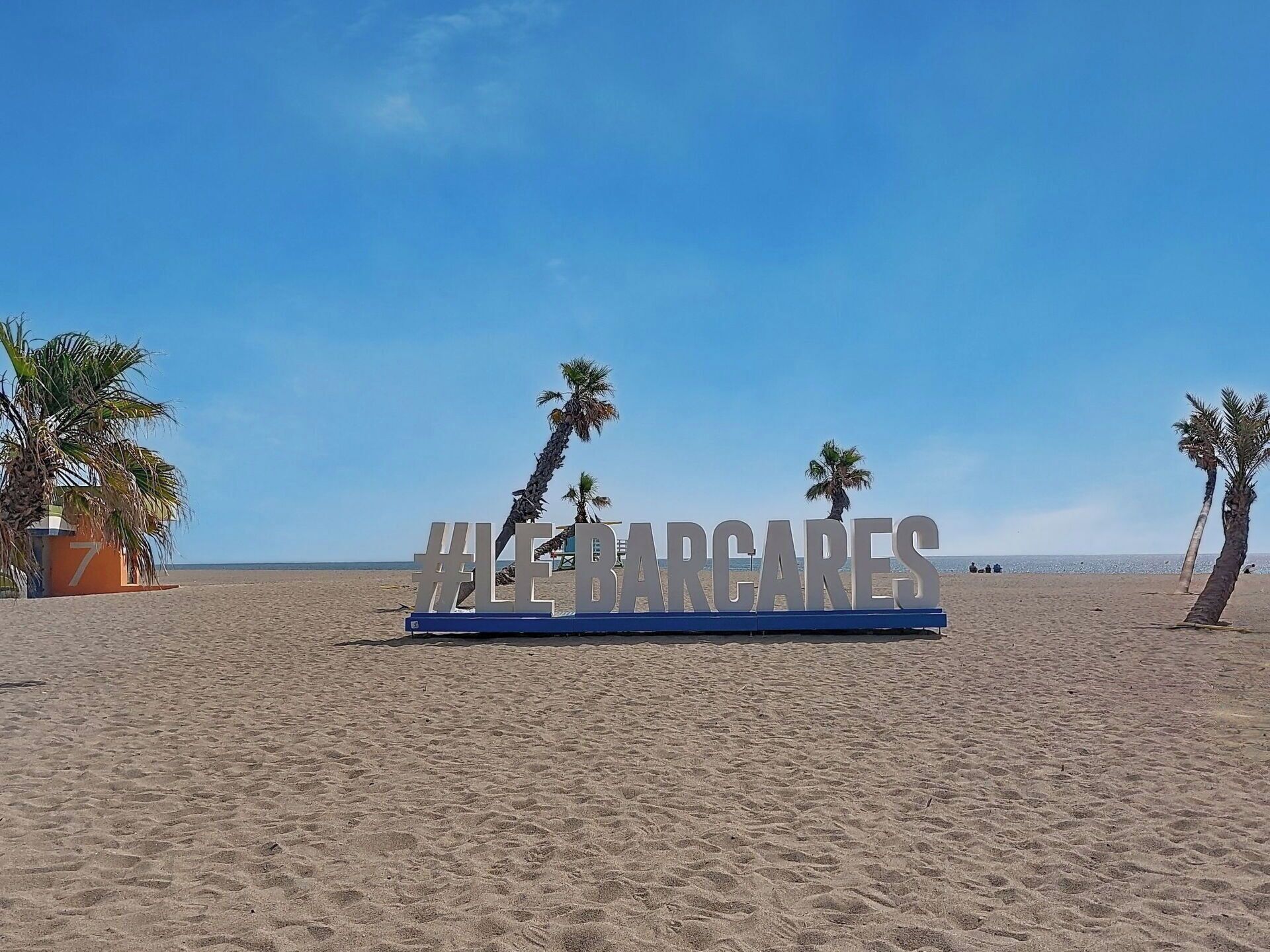 Ein Strand mit einem Schild, auf dem '#LEBARGUES' steht, und Palmen.