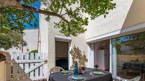 An outdoor patio with a table set for dining, surrounded by chairs, a white fence, and a tree providing shade. - Nice apartment for 4 guests with WIFI, TV and terrace (Port Leucate)