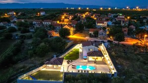 A residential area with houses, a swimming pool, and a well-lit patio area. - Stunning private villa for 8 guests with A/C, hot tub, WIFI, private pool, TV and terrace (Zadar)