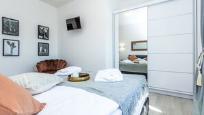 A modern hotel room with a bed, a brown armchair, a flat-screen TV mounted on the wall, and a sliding door closet. - Stunning private villa for 8 guests with A/C, hot tub, WIFI, private pool, TV and terrace (Zadar)