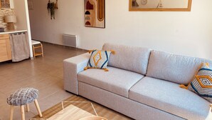 A modern living room with a grey sofa, two patterned throw pillows, a wooden side table, and a woven rug. - Maison Moderne Avec Jardin (Saint Xandre)