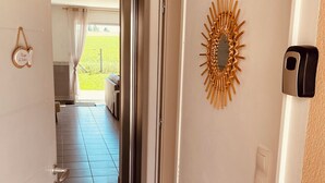 A hallway with a tiled floor, a door with a handle, a wall-mounted light fixture, and a decorative sunburst wall art piece. - Maison Moderne Avec Jardin (Saint Xandre)