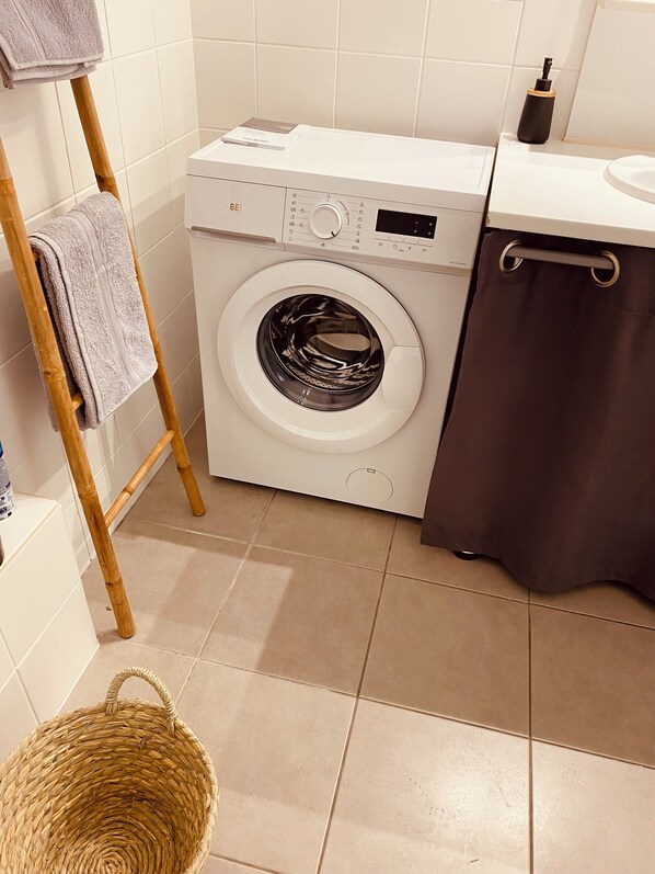 A compact laundry area with a front-loading washing machine, a drying rack, and a basket. - Maison Moderne Avec Jardin (Saint Xandre)