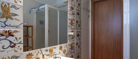 A bathroom with a white sink, wooden cabinet, and a mirror. The walls are decorated with floral tiles.