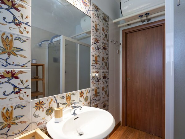 A bathroom with a white sink, wooden cabinet, and a mirror. The walls are decorated with floral tiles.