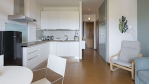 Une cuisine moderne avec des meubles blancs, un réfrigérateur noir et un coin repas comprenant une table et des chaises blanches.